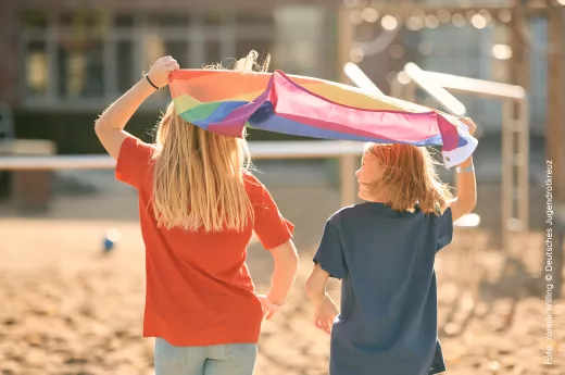 Zwei Kinder mit Regenbogenfahne auf einem Spielplatz